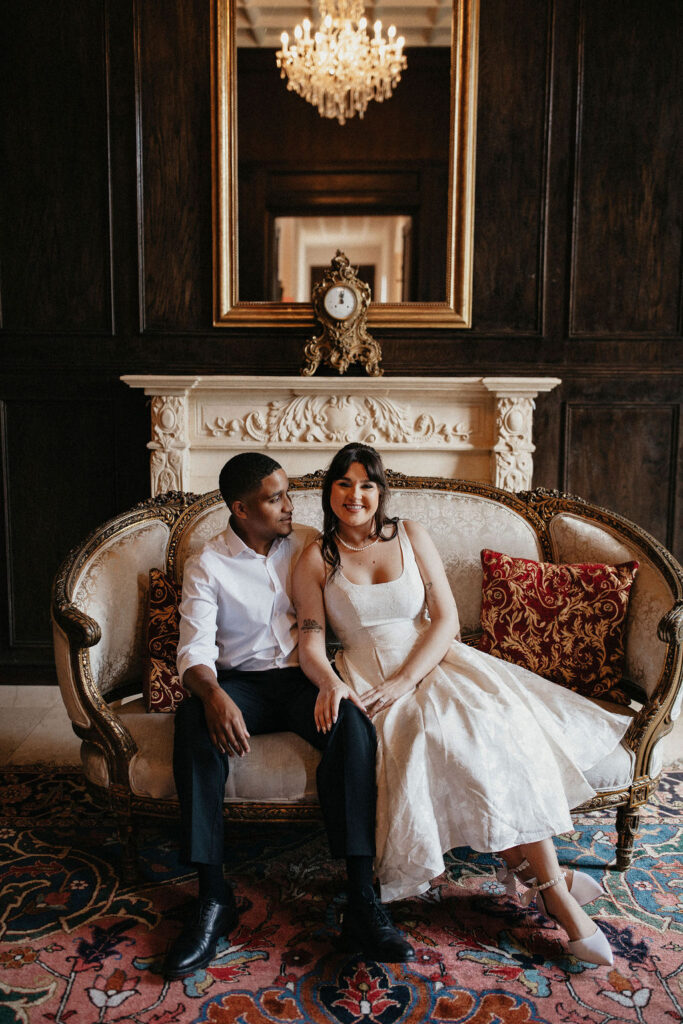 An engaged couple is seated on a French inspired couch during their Chateau Nouvelle Houston TX engagement session