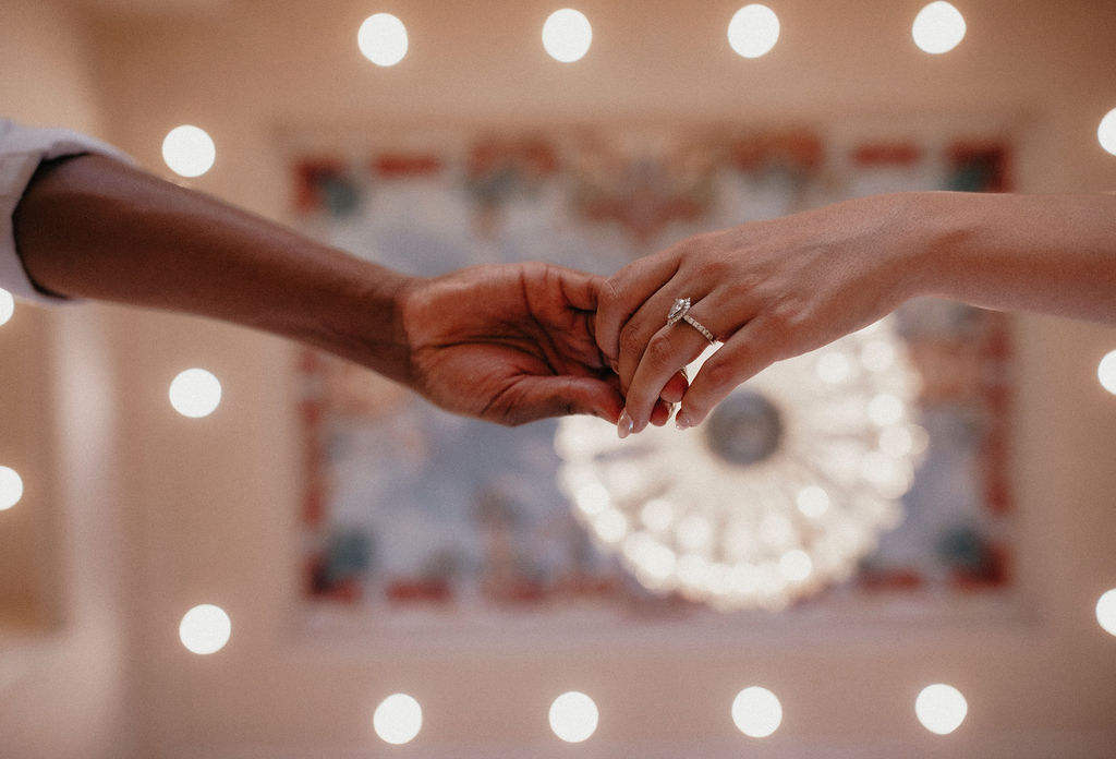 A photo taken during a Chateau Nouvelle engagement session showcases a couple holding hands beneath the imported Tiffany ceiling