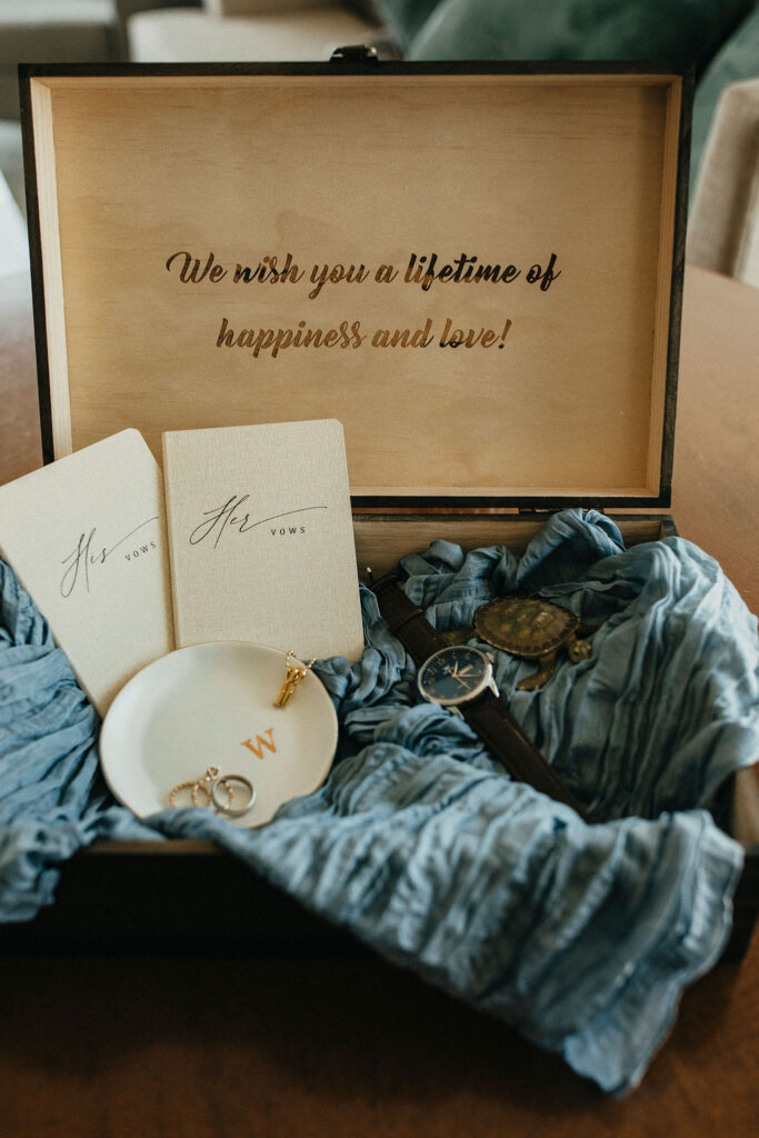 Wedding details are photographed displaying vow notebooks, wedding rings, and the groom's watch atop blue fabric at a trattoria lisina wedding