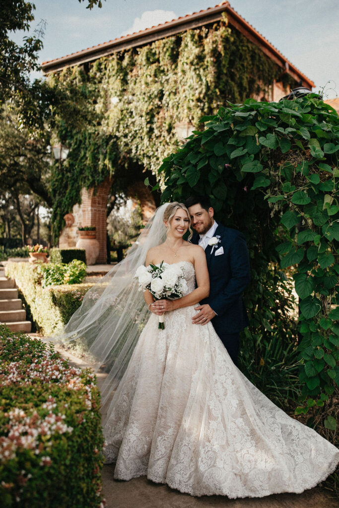 A bridal portrait taken in Austin TX features a bride in a lace gown leaning into her husband in a black tux taken outside of their texas hill country elopement