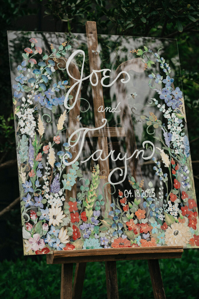 A hand-painted floral sign welcomes guests to a wedding at Pecan Springs Ranch in Austin, TX