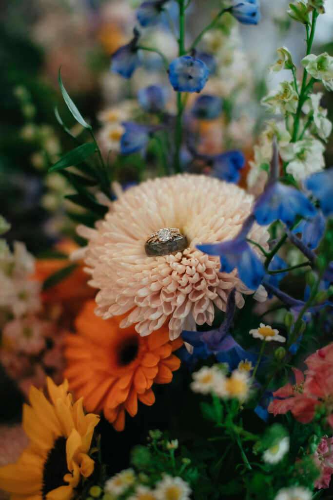 Wedding rings are photographed on a colorful bouquet at a wedding at Pecan Springs Ranch Austin Texas