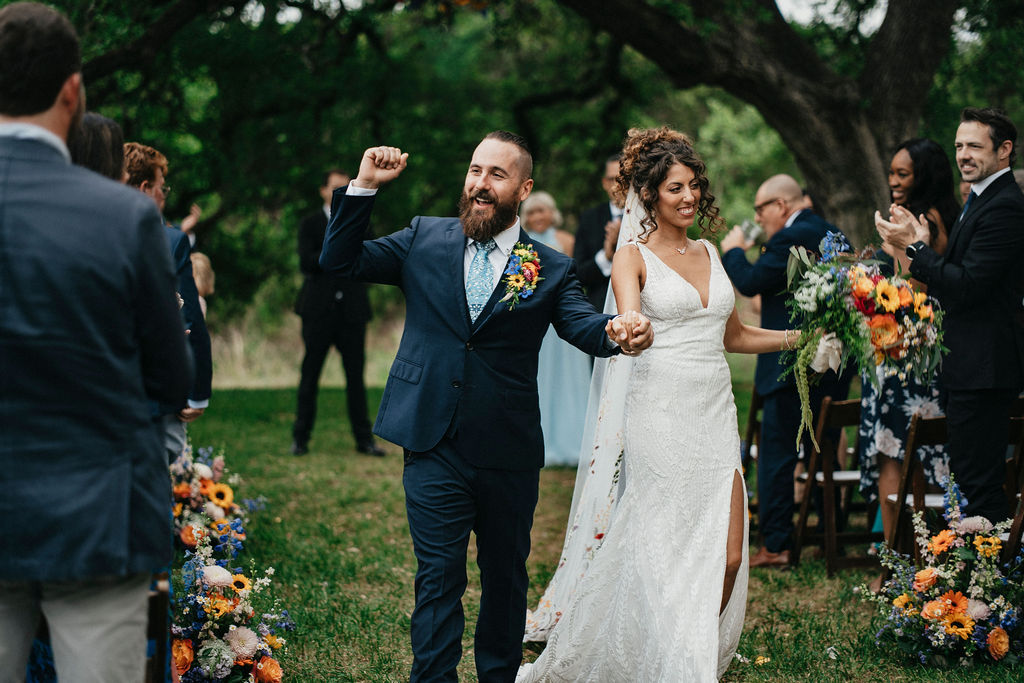 Newlyweds celebrate as they walk hand-in-hand down the aisle of their Austin TX wedding at Pecan Springs Ranch