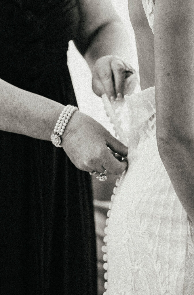 The mother of the bride assists her daughter with the buttons of her wedding dress at Pecan Springs ranch, one of the outdoor wedding venues in texas