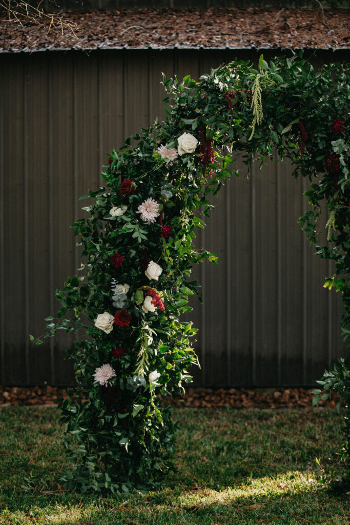 A floral arch decorated in deep red & white blooms is photographed at a wedding in Houston 