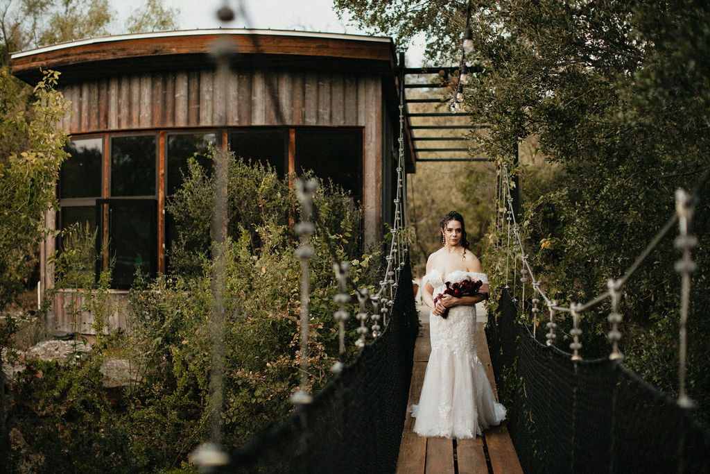 A bride poses for a bridal portrait on the suspension bridge at a Spicewood TX treehouse venue
