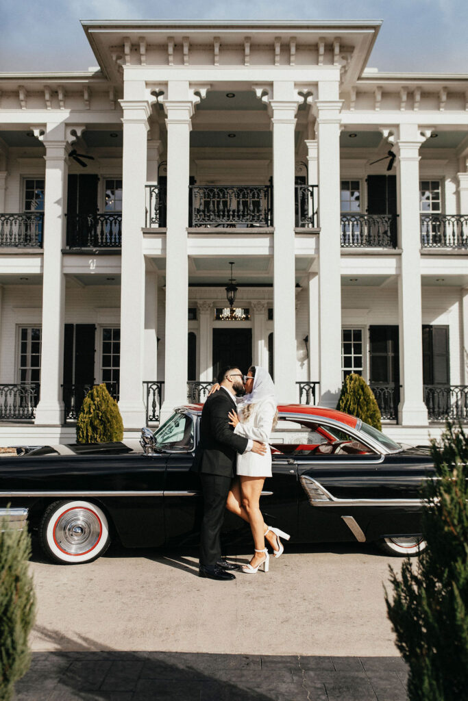 A couple pose before a vintage car parked outside Sandlewood Manor for their Houston engagement photos 