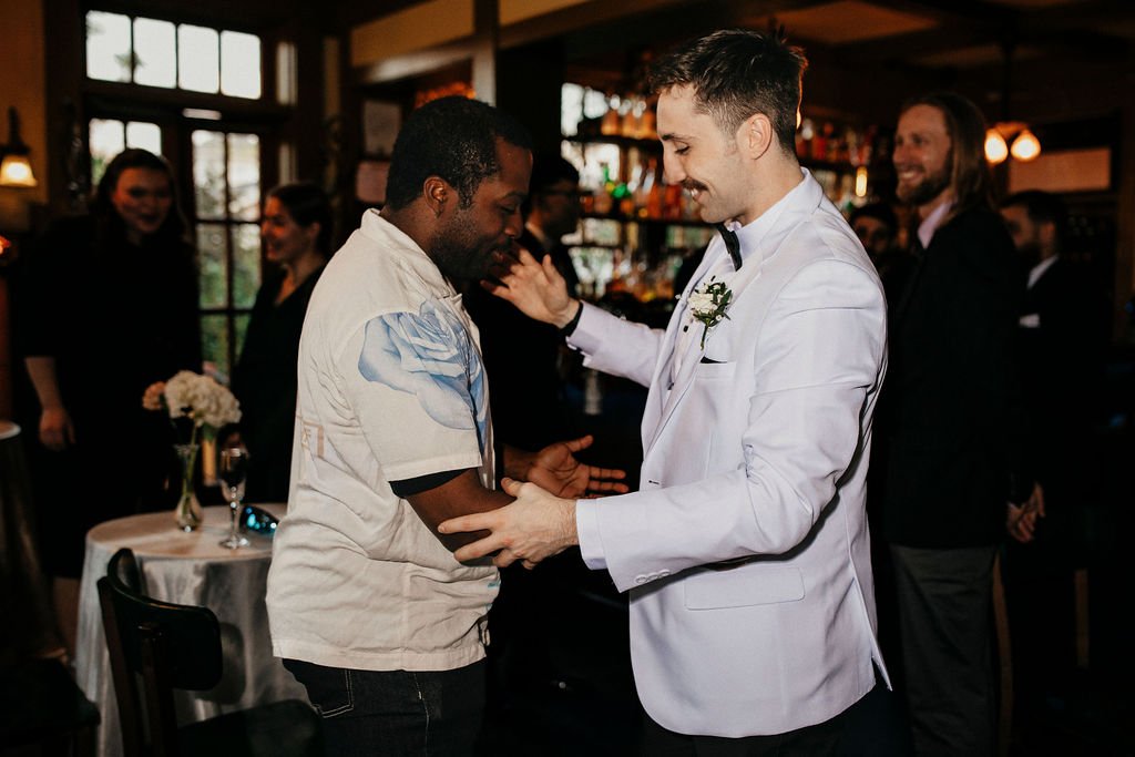 A groom leans in to hug a guest at his Avant Garden wedding in Houston, TX. 