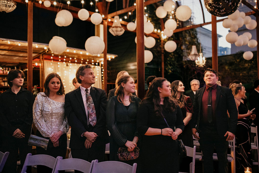 Guests stand beneath paper lanterns as the bride walks down the aisle at a nighttime avant garden houston wedding. 