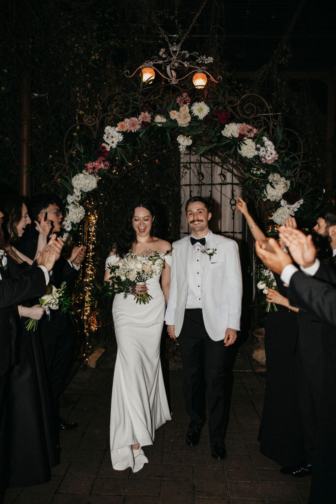 Newlyweds smile beneath a floral arch at their avant garden houston wedding.