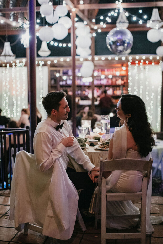 Newlyweds hold hands deep in conversation beneath paper lanterns and string lights at their avant garden houston wedding reception. 