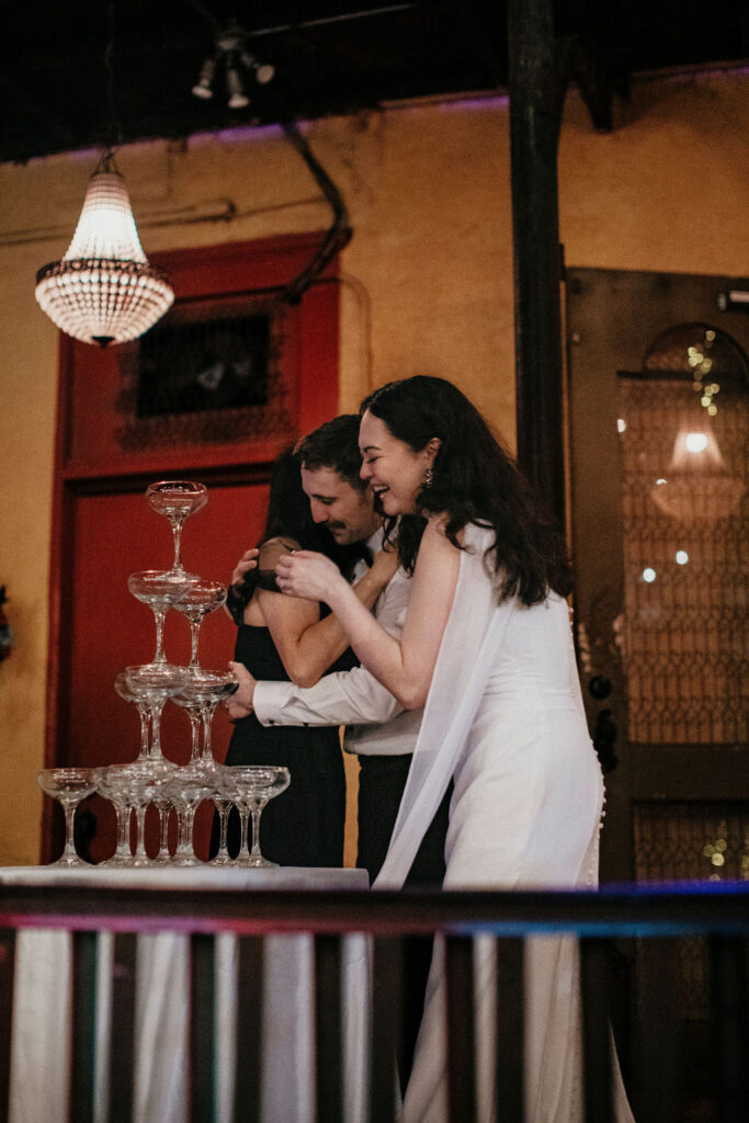 Newlyweds hug a guest next to a champagne tower at their avant garden houston wedding. 