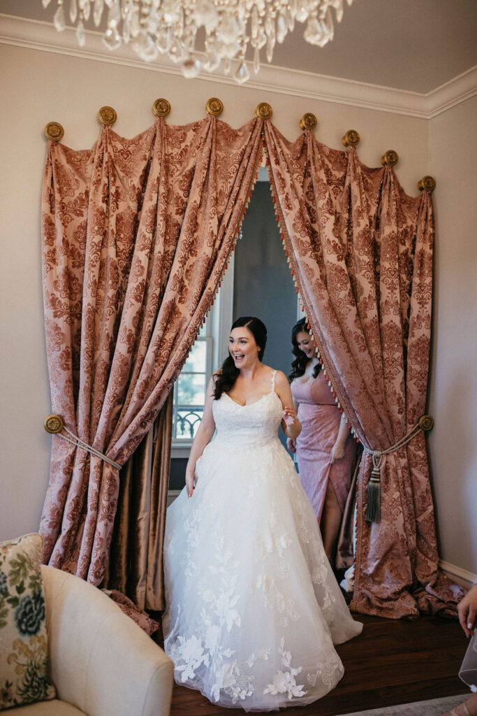 A bride smiles as she shows her bridesmaids her finished bridal look before her Sandlewood Manor wedding. 