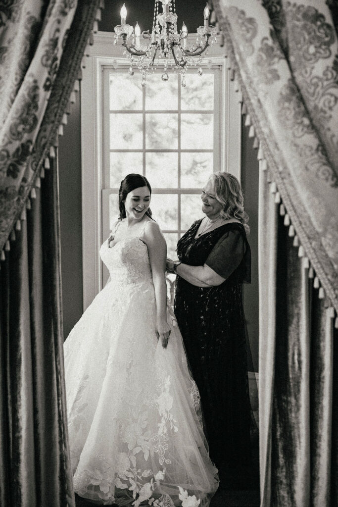 A b+w image depicts a mother helping her daughter get ready for her Sandlewood Manor wedding. 