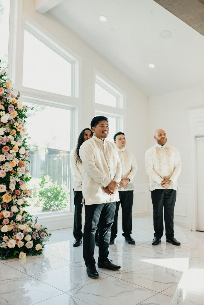 A groom smiles as he watches his bride walk down the aisle at their Sandlewood Manor wedding. 