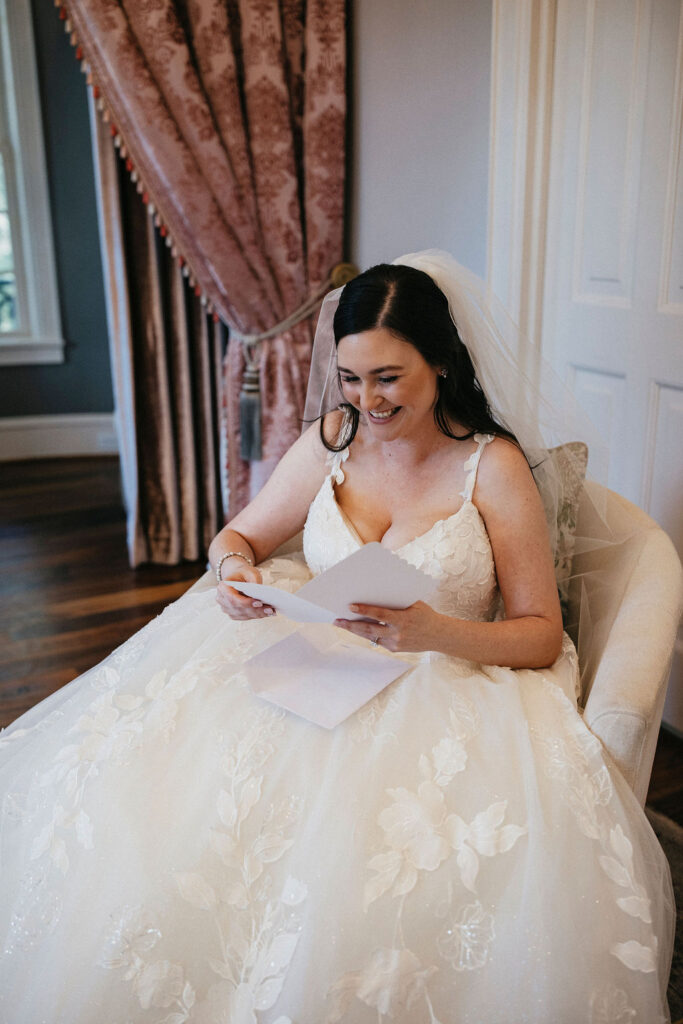A Texas bride smiles as she reads a personal note from her groom before their Sandlewood Manor wedding. 