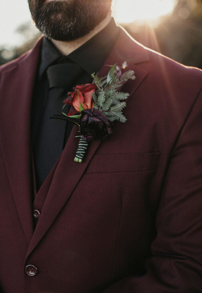 A gothic boutonniere set against a maroon tux jacket is photographed at a Texas ranch wedding.