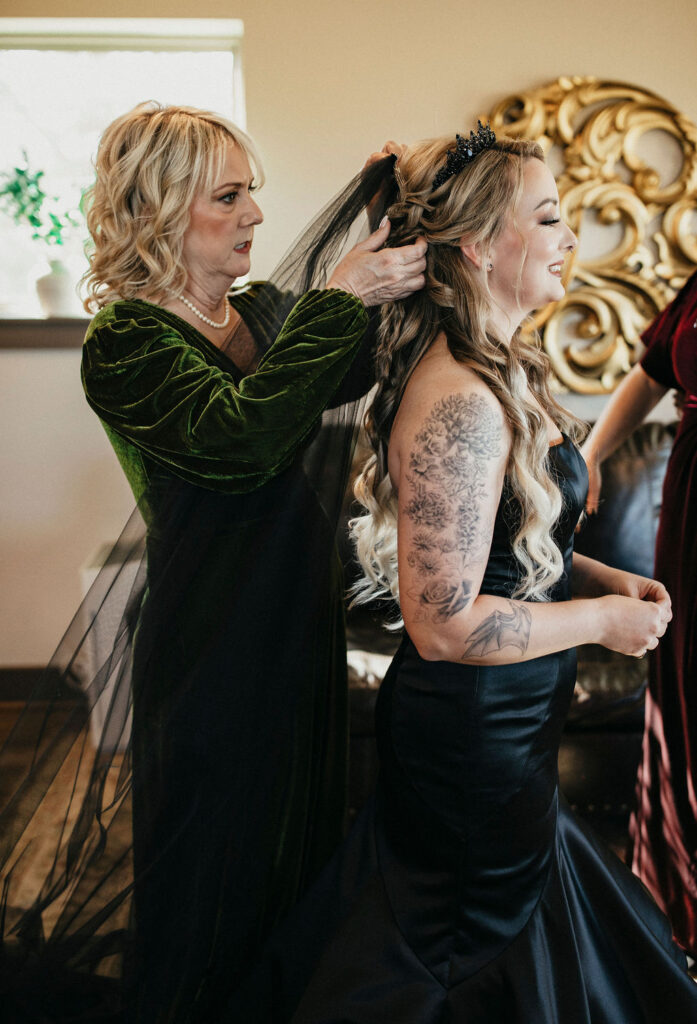 A bride has help with her black wedding veil before her Gothic western ranch wedding in Texas.
